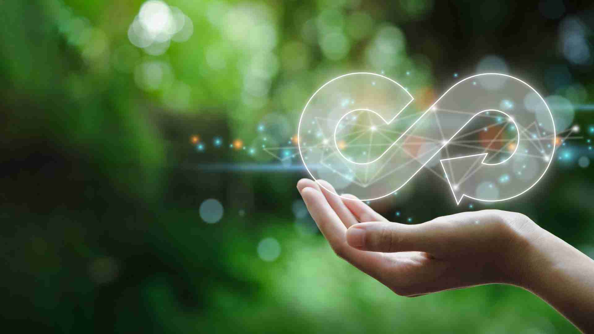 A hand holding a glowing infinity symbol against a green background